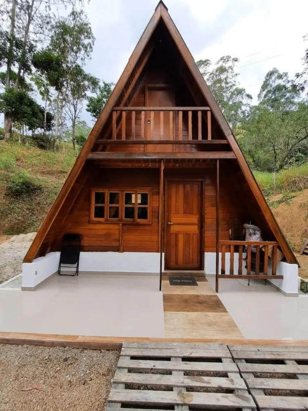 Chalé A-frame completo em madeira escura com base branca e varanda