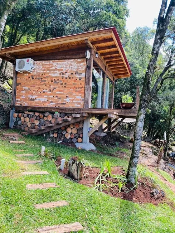 Cabana rústica elevada com madeira e tijolos em encosta verde
